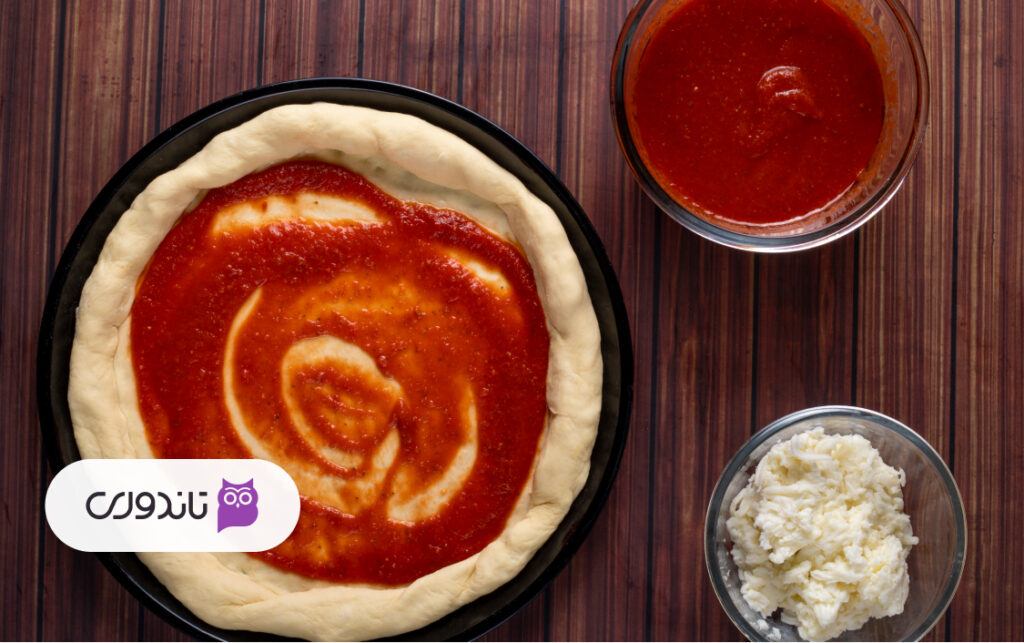 مرحله ششم: پخش‌کردن سس مارینارا روی خمیر پیتزا پپرونی